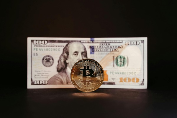 Bitcoin coin with a hundred-dollar banknote on black
