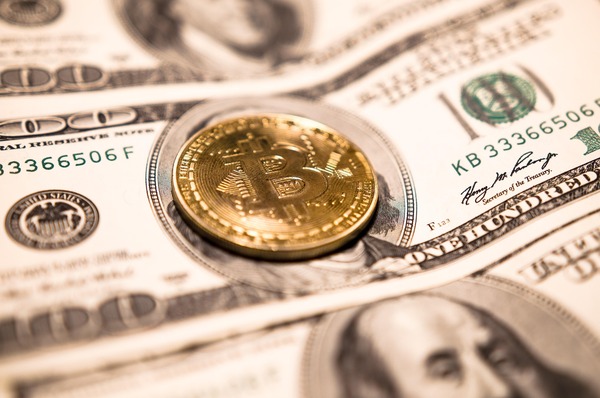 Gold Bitcoin coin on hundred-dollar bills
