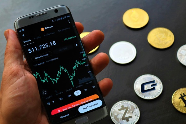Hand holding a phone with a price chart near coins