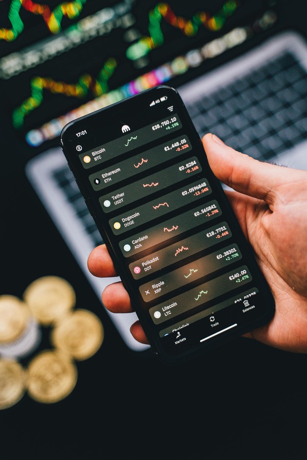 Hand holding a smartphone with a crypto trading app above coins