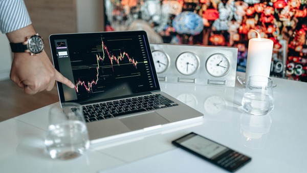 Hand pointing at a trading chart on a laptop screen