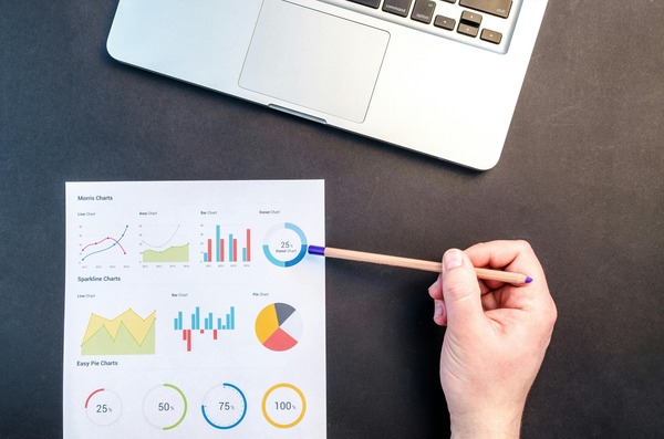 Hand pointing at printed financial charts next to a laptop