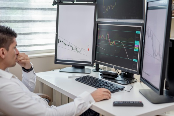 Trader analysing charts on multiple monitors
