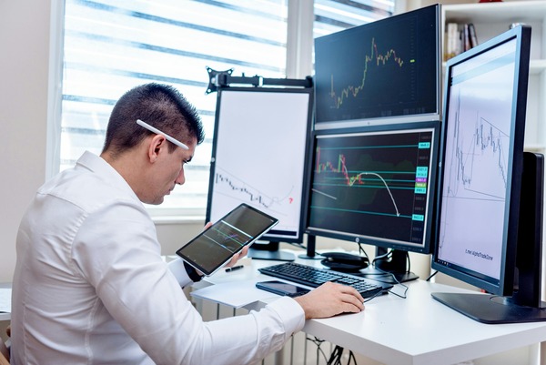 Trader with a tablet in front of monitors with charts
