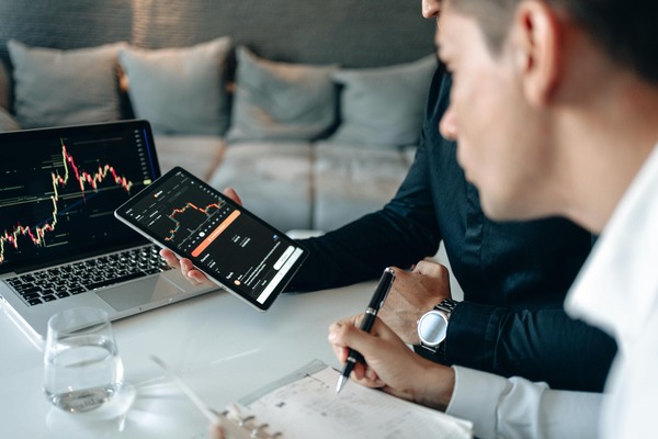 Two people reviewing trading charts on a tablet and laptop